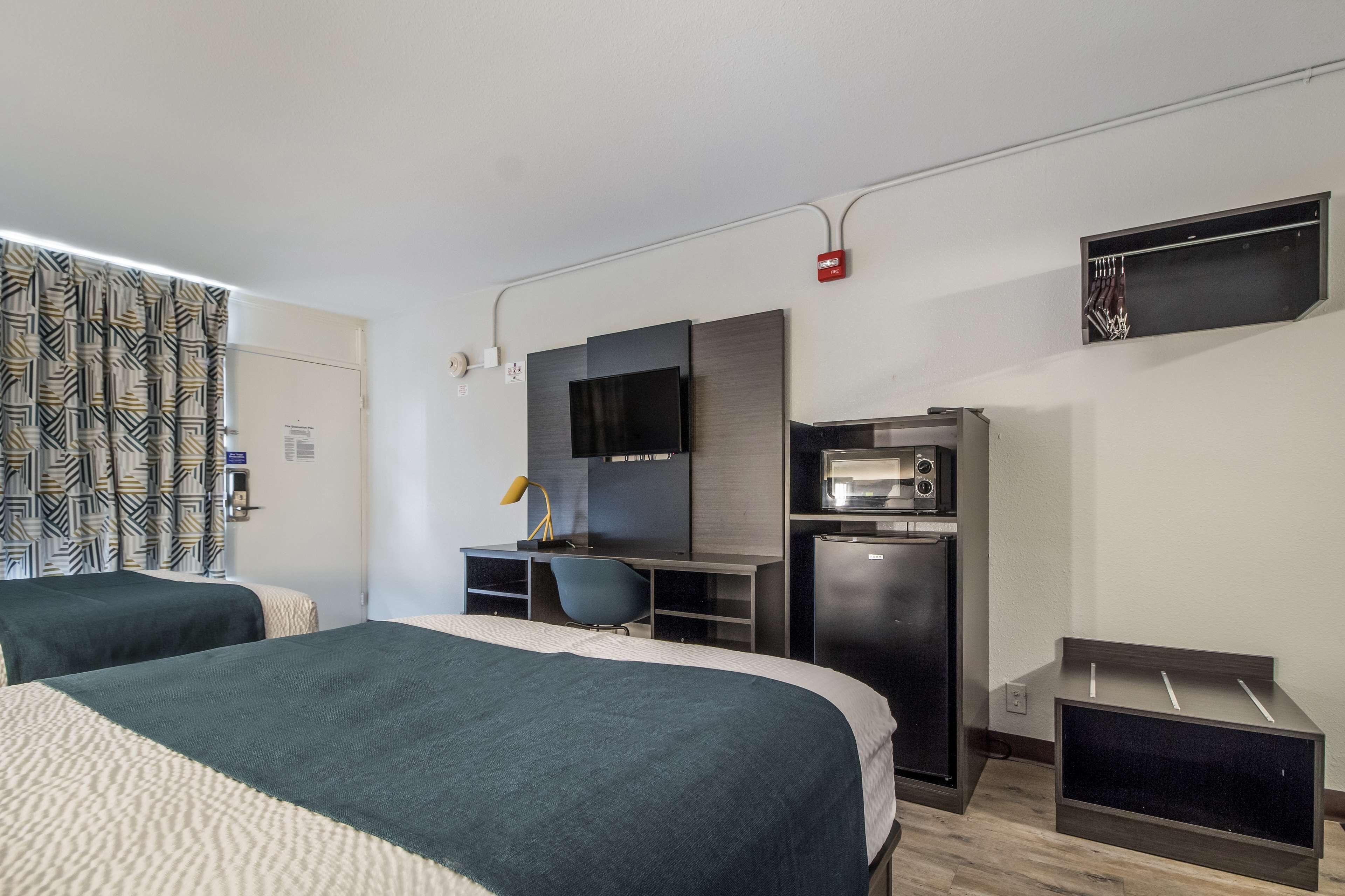 A hotel room with two beds, a desk with a computer, a microwave, and a TV.