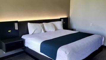 A neatly made bed with white linens and a dark blue throw blanket, flanked by two bedside tables with black surfaces and a headboard with integrated lighting.