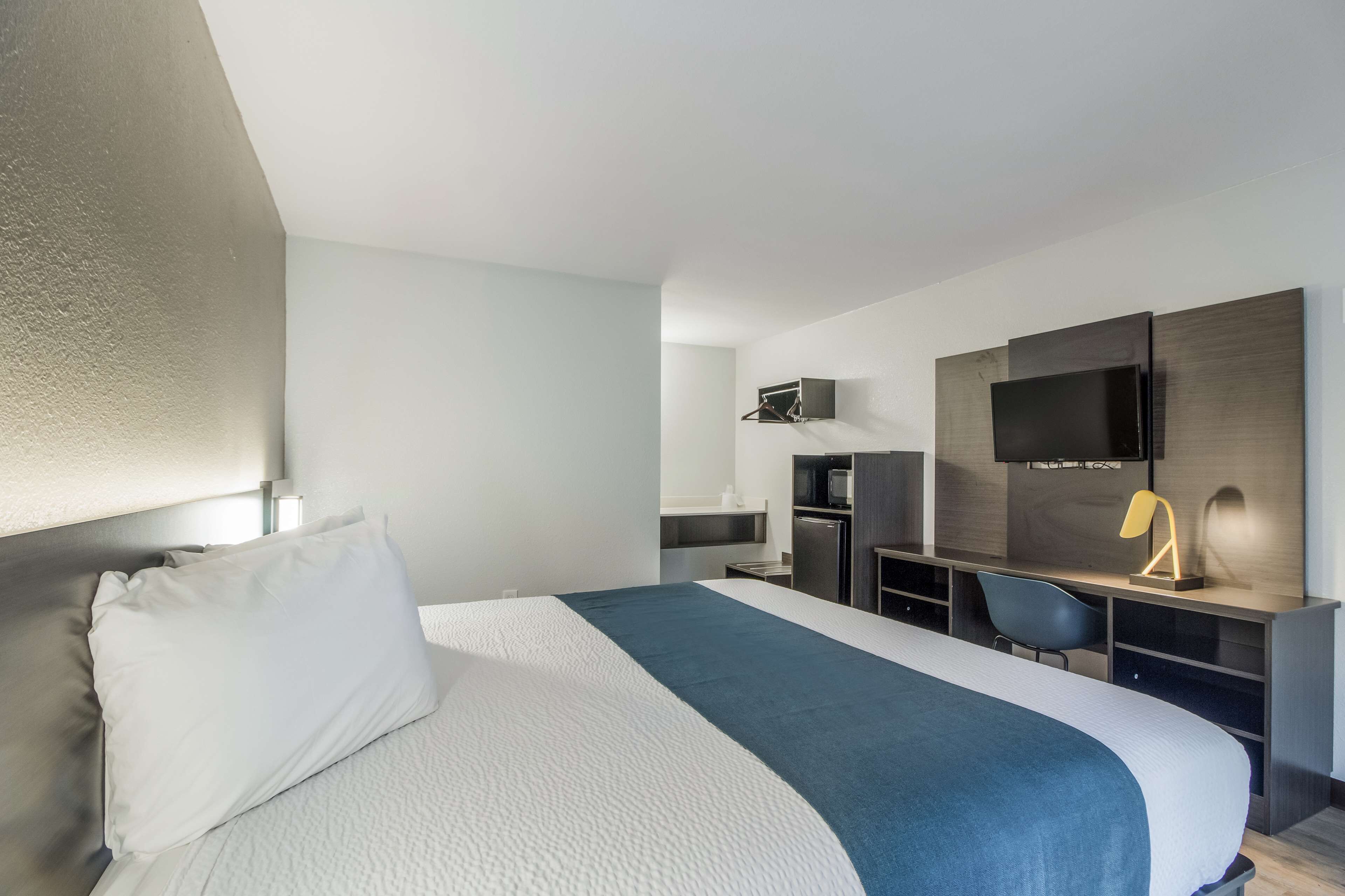 Una habitación de hotel moderna con una cama grande, un escritorio, una silla, un televisor de pantalla plana y una kitchenette pequeña.