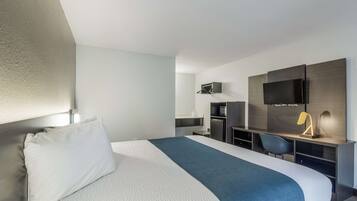 Una habitación de hotel moderna con una cama grande, un escritorio, una silla, un televisor de pantalla plana y una kitchenette pequeña.