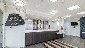 A reception area with a modern design, including a reception desk, a large number '6' sign, and a motivational quote on the wall. - Motel 6 Groves, TX (Groves)