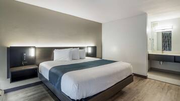A modern hotel room with a large bed, bedside tables, a built-in bench, a mirror, and a small shelf.