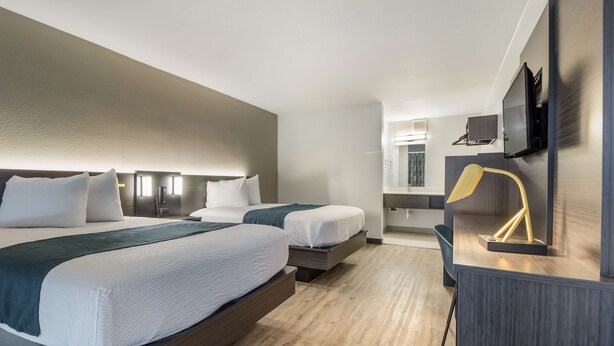 A hotel room with two beds, a desk, a chair, a TV, and a mirror. - Motel 6 Groves, TX (Groves)