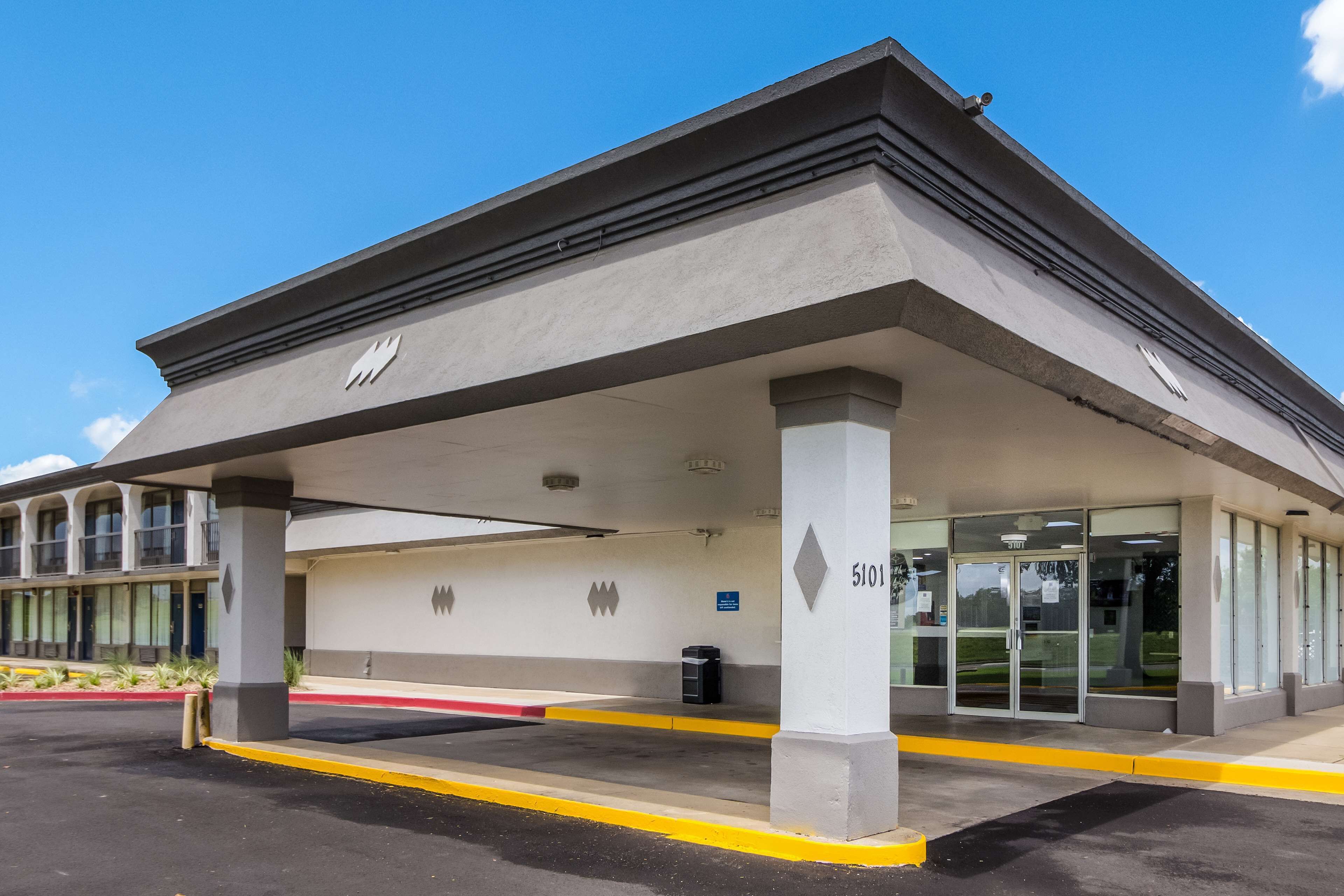 A building with a covered parking area, columns, and a glass entrance.