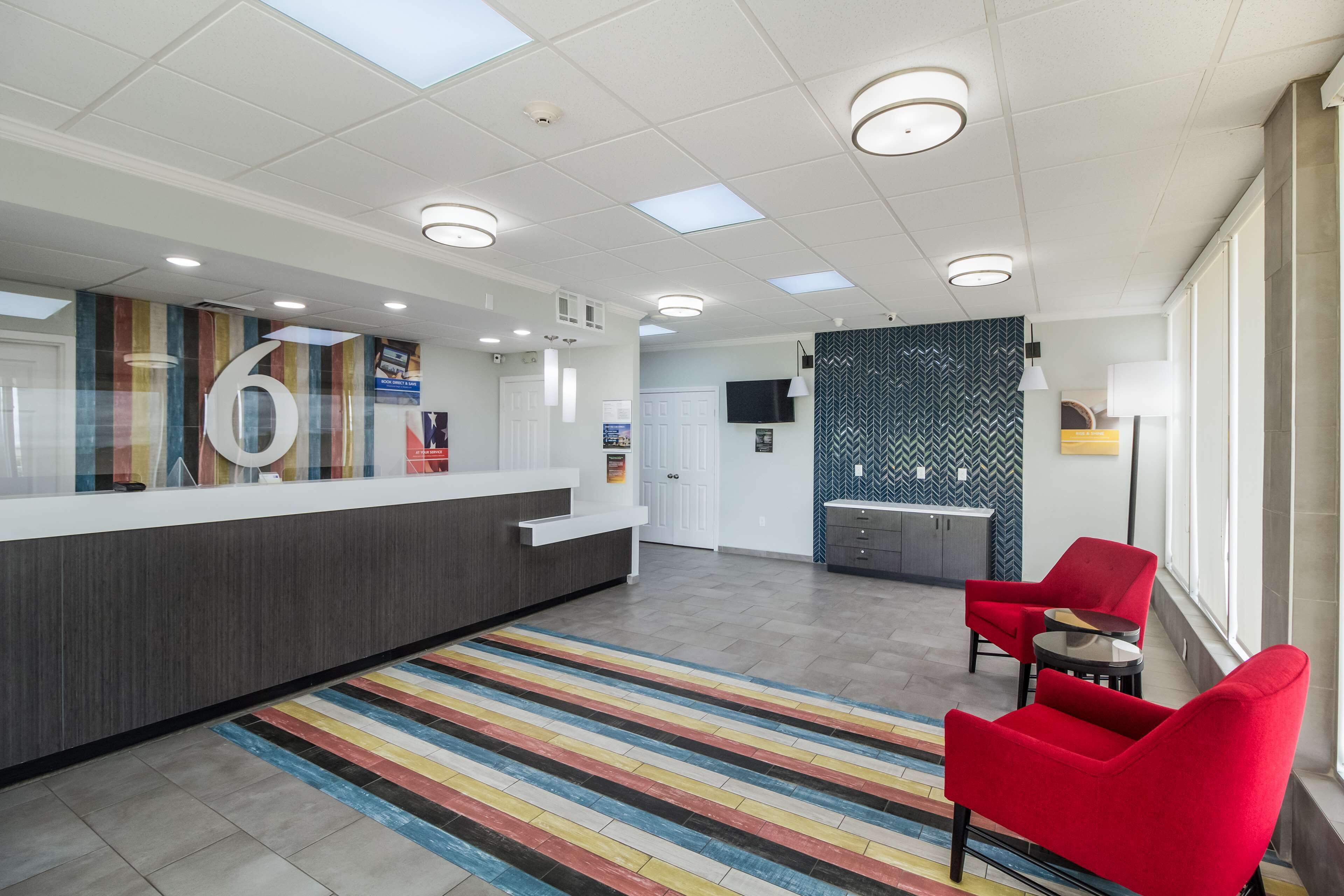 Un espace d’accueil avec un comptoir, un grand panneau portant le chiffre « 6 », un tapis à rayures, des chaises rouges et un mur orné d’un motif en chevrons.