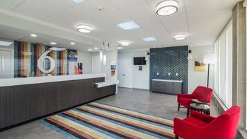 Un espace d’accueil avec un comptoir, un grand panneau portant le chiffre « 6 », un tapis à rayures, des chaises rouges et un mur orné d’un motif en chevrons.