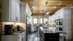 A modern kitchen with white cabinetry, a central island, stainless steel appliances, and a wooden ceiling.