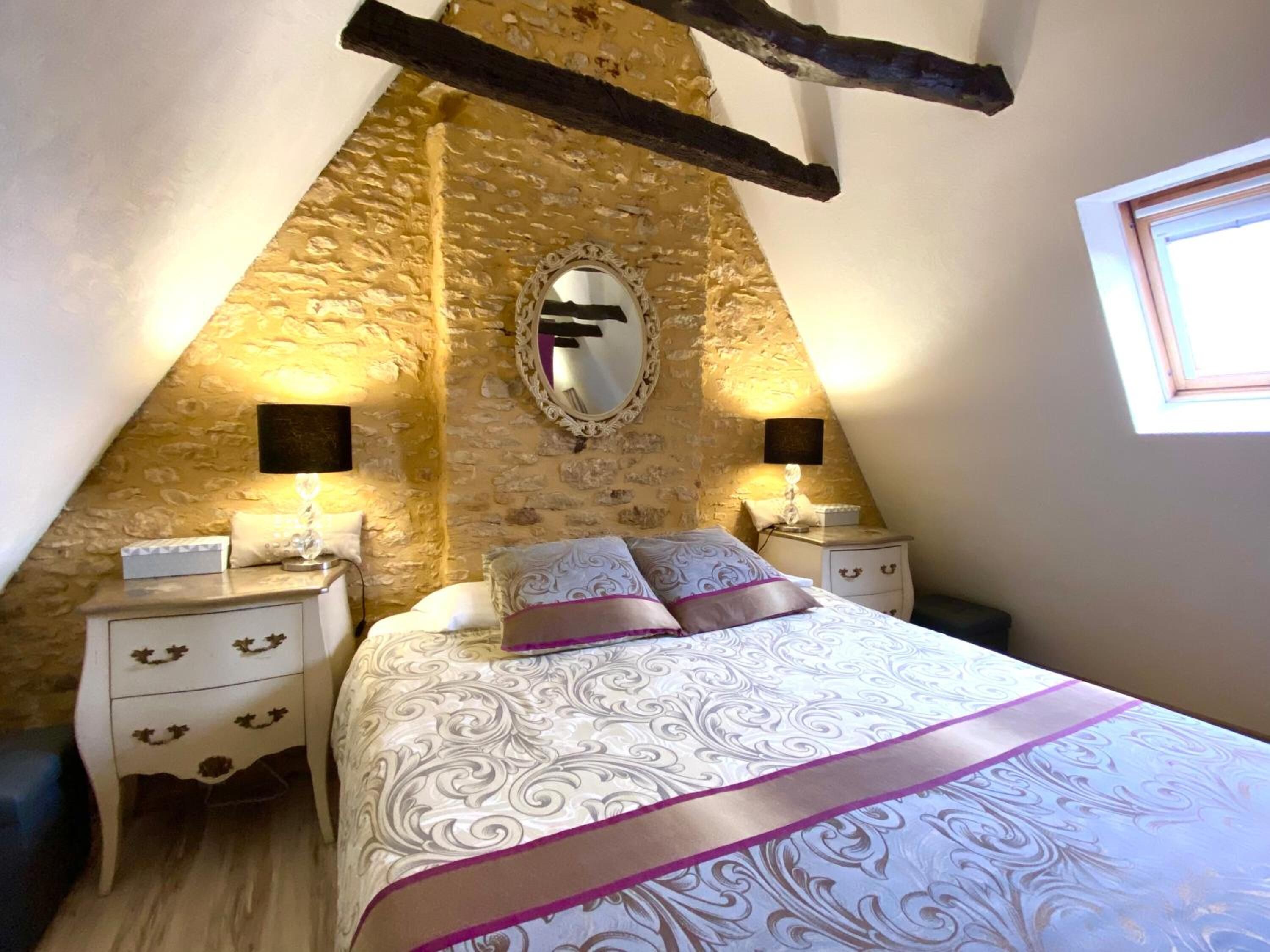 Un dormitorio con pared de piedra, una cama con ropa de cama estampada, dos mesitas de noche y un espejo.