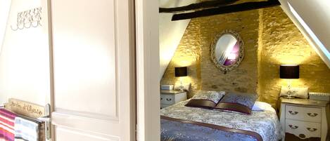 A bedroom with a stone wall, a bed with patterned bedding, two bedside tables with lamps, and a mirror on the wall.