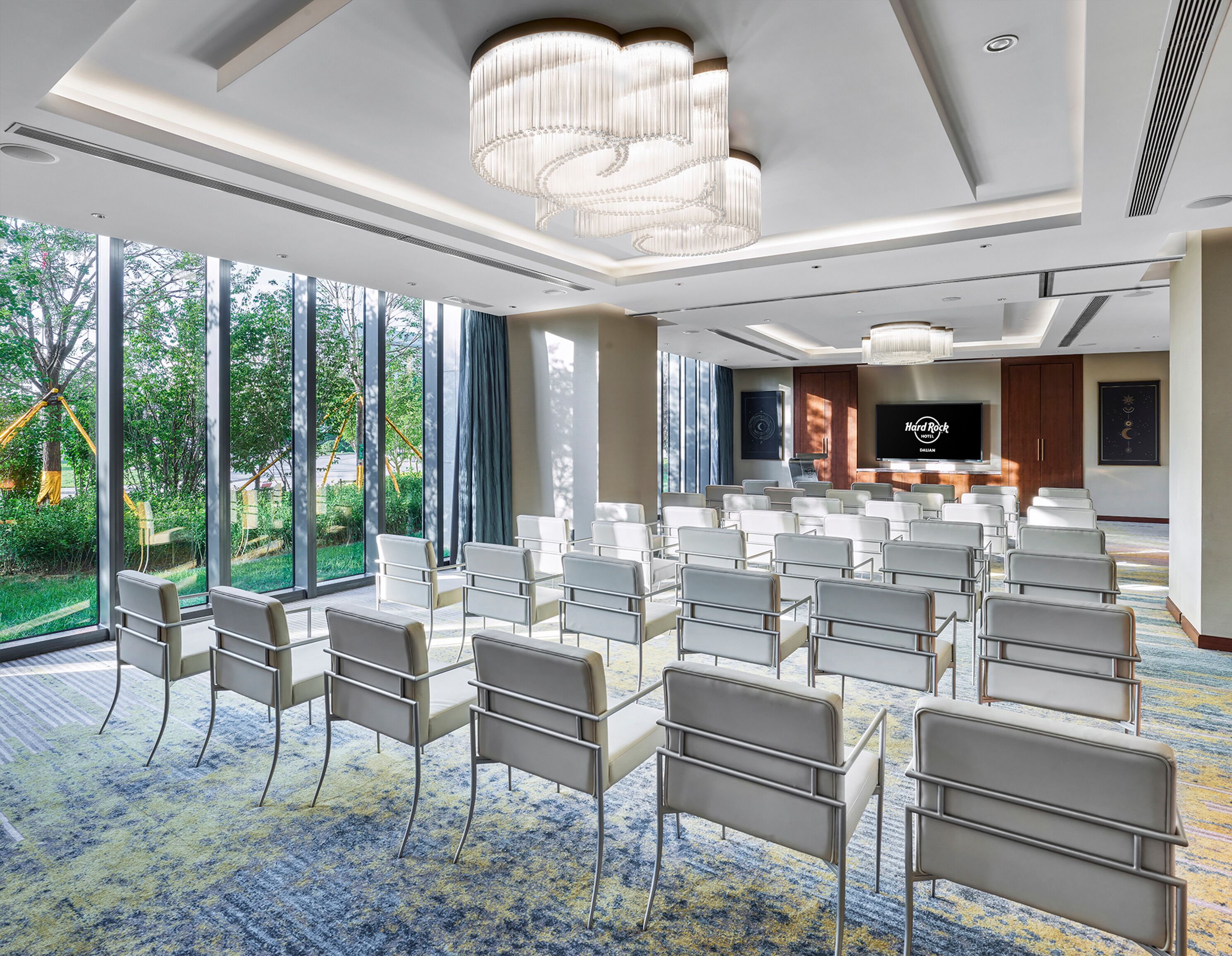 A conference room with rows of white chairs, a large chandelier, and a television screen displaying 'Hard Rock'.