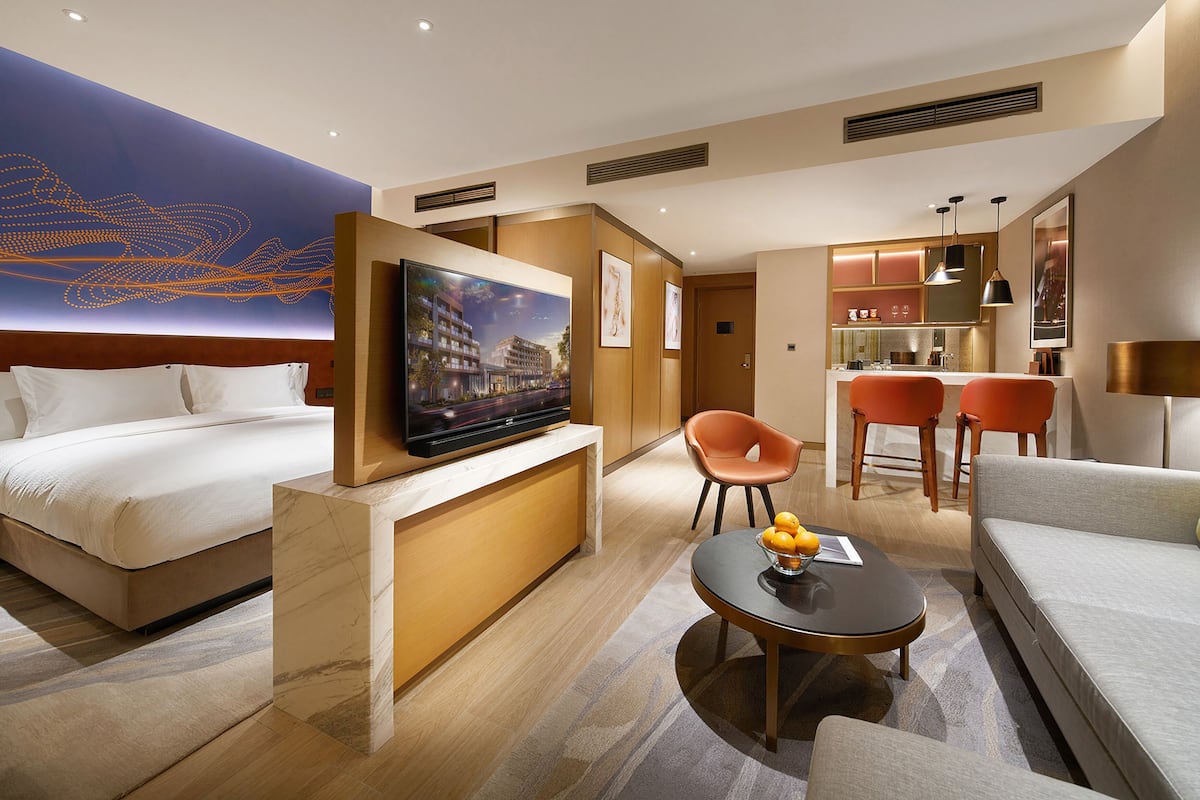 Habitación de hotel con cama, televisión, zona de estar con mesa y sillas, y kitchenette.