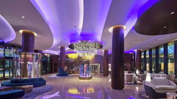 Eine moderne Lobby mit einem zentralen Kronleuchter, Sitzbereichen und einer Glastheke mit Schaufensterpuppen.