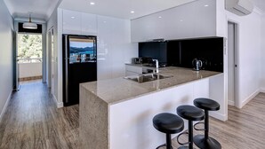 A modern kitchen with a central island, bar stools, and a view through the window. - Whitsunday Apartment West 1002 (Hamilton Island)