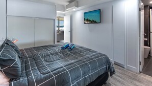 A bedroom with a bed, a ceiling fan, a painting, and a bathroom door. - Whitsunday Apartment West 1002 (Hamilton Island)