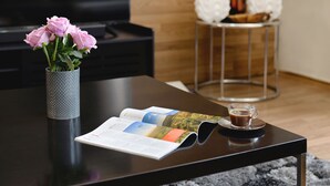 A black table with a magazine, a cup of coffee, and a vase with pink flowers. - Kimberley House (Cape Town)
