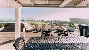 Une terrasse sur le toit, avec une table et des chaises, une vue sur la ville et un espace abrité doté d’une rambarde.