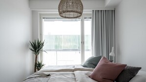 A bedroom with a large bed, a hanging light fixture, a potted plant, and a view through a window. - SleepWell Apartments Espoo Near Helsinki City Center (Espoo)