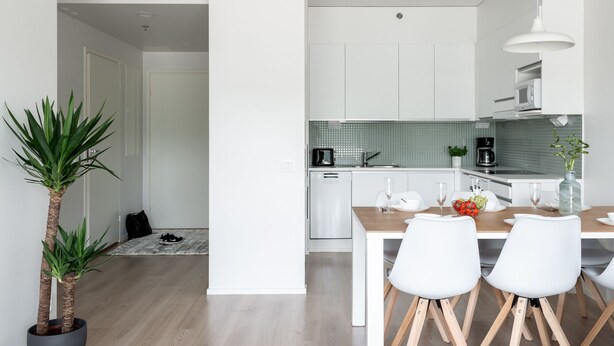 A modern kitchen with white cabinets, a dining area with two white chairs, a coffee maker, and a potted plant. - SleepWell Apartments Espoo Near Helsinki City Center (Espoo)