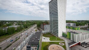 A modern high-rise building with a rectangular shape and a flat roof, surrounded by a landscaped area with a circular garden and seating. - SleepWell Apartments Espoo Near Helsinki City Center (Espoo)