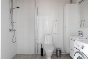 Un baño moderno con cabina de ducha de vidrio, inodoro, lavadora y lavabo con espejo.