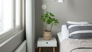 A bedroom with a radiator, a bedside table with a lamp, a plant, and a bed with pillows. - SleepWell Apartments Katajanokka (Helsinki)
