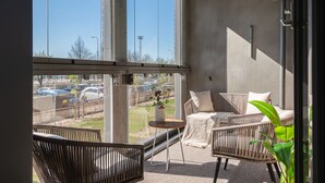 A balcony with wicker furniture, a small table with a vase, and a view of a parking lot. - SleepWell Apartments Katajanokka (Helsinki)