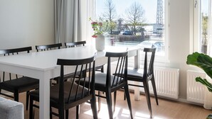 A modern dining area with a white table and black chairs, large windows with a view of the Eiffel Tower, and a hanging light fixture. - SleepWell Apartments Katajanokka (Helsinki)