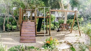 A wooden play structure with a slide and a swing set in a garden with trees and plants. - 438 St Martini (Cape Town)