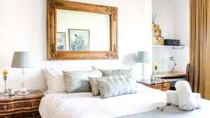 A neatly made bed with white linens and multiple pillows, a wooden nightstand with a lamp, and a framed mirror on the wall. - 438 St Martini (Cape Town)
