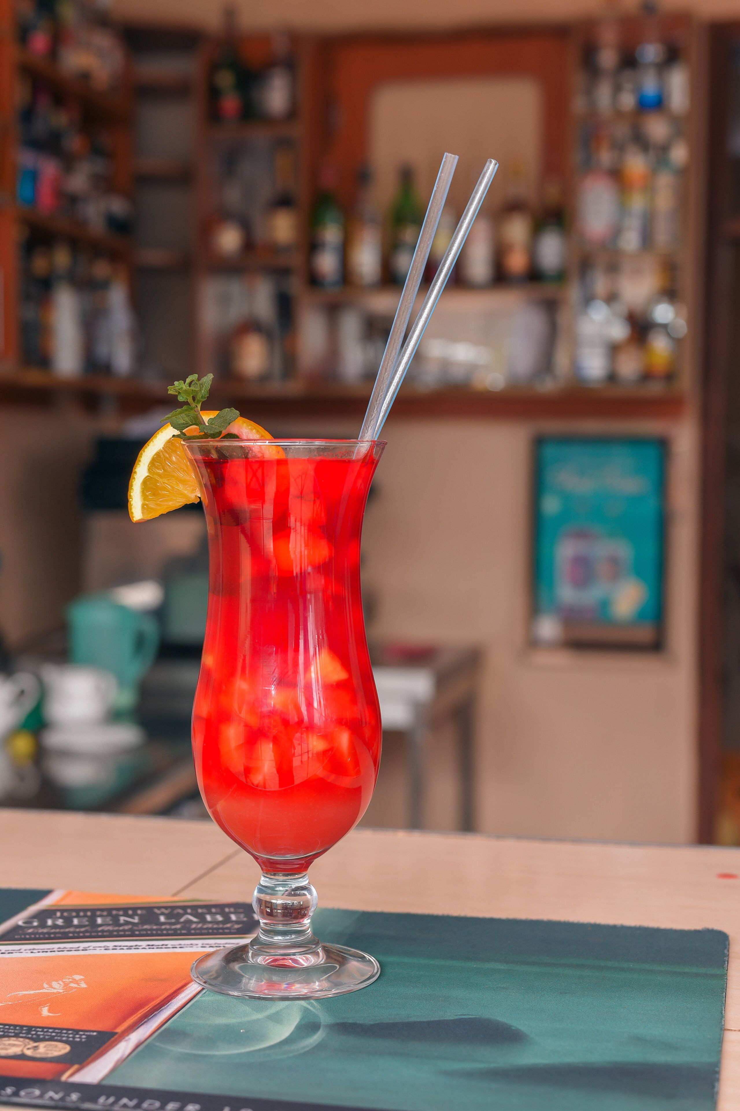 Punainen cocktail-lasi, jossa on juomaa, koristeltuna appelsiiniviipaleella ja mintunlehdillä, pöydällä, jonka päällä on ruokalista.