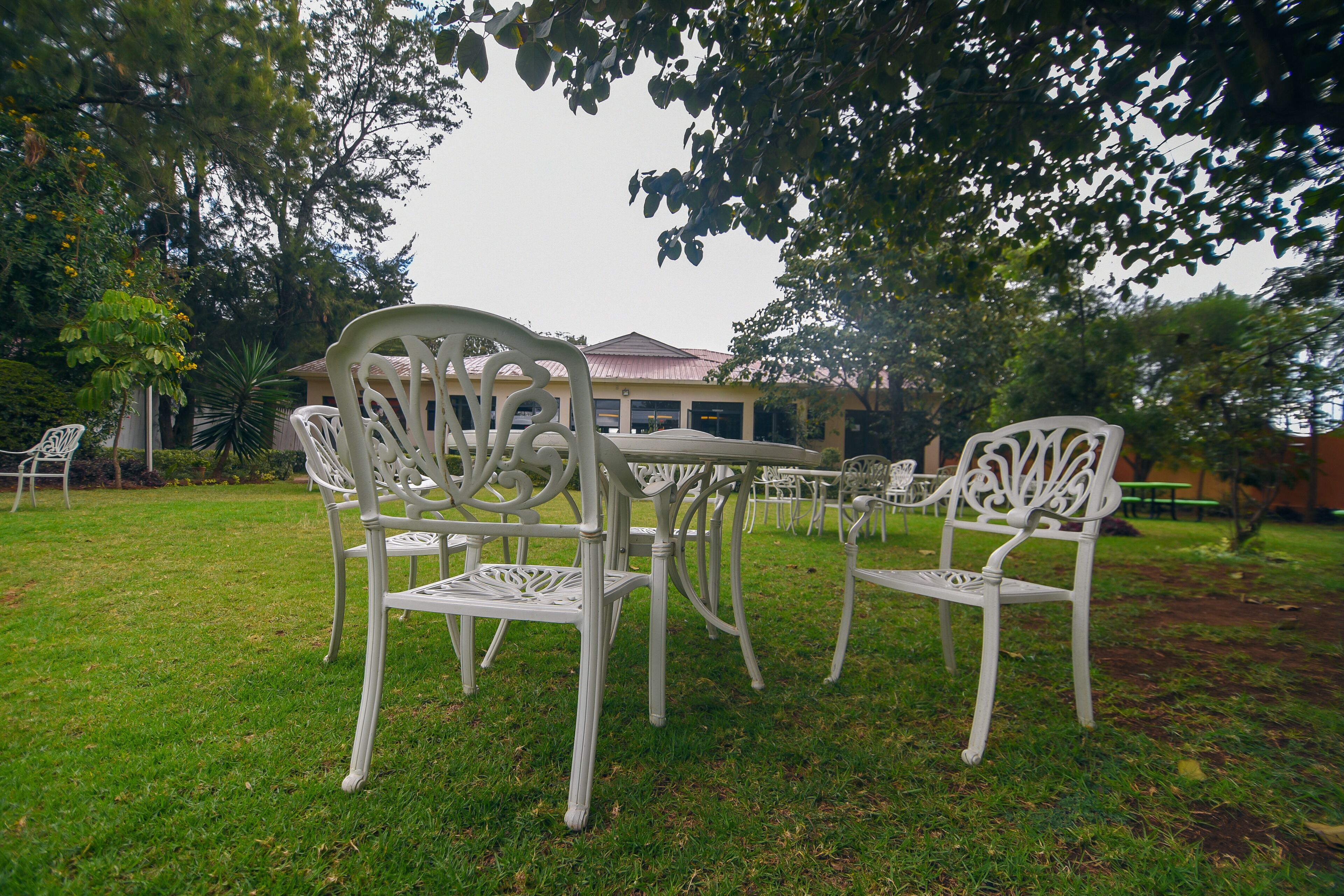 A white outdoor seating area with a table and chairs, surrounded by grass and trees.
