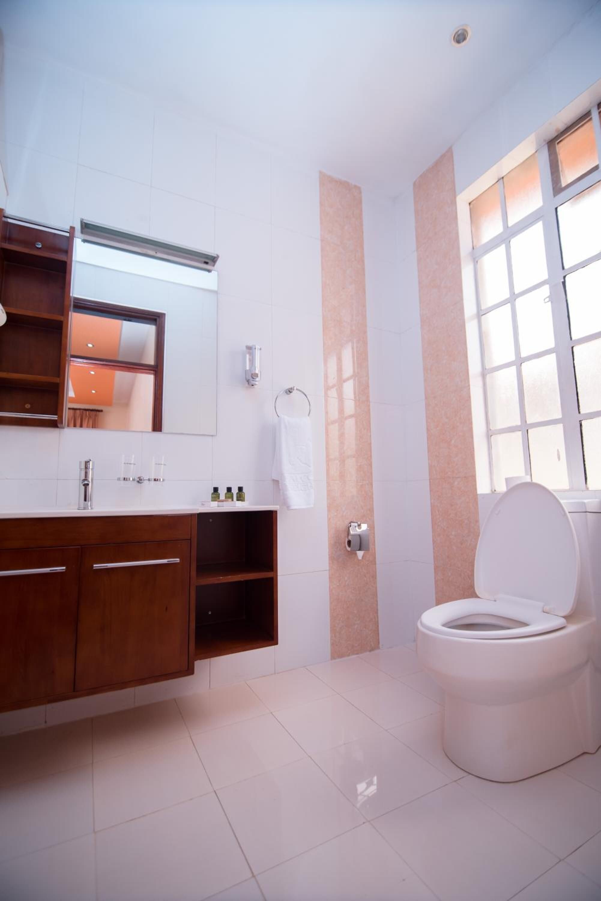 Un baño moderno con inodoro blanco, tocador con espejo y ventana que proporciona luz natural.