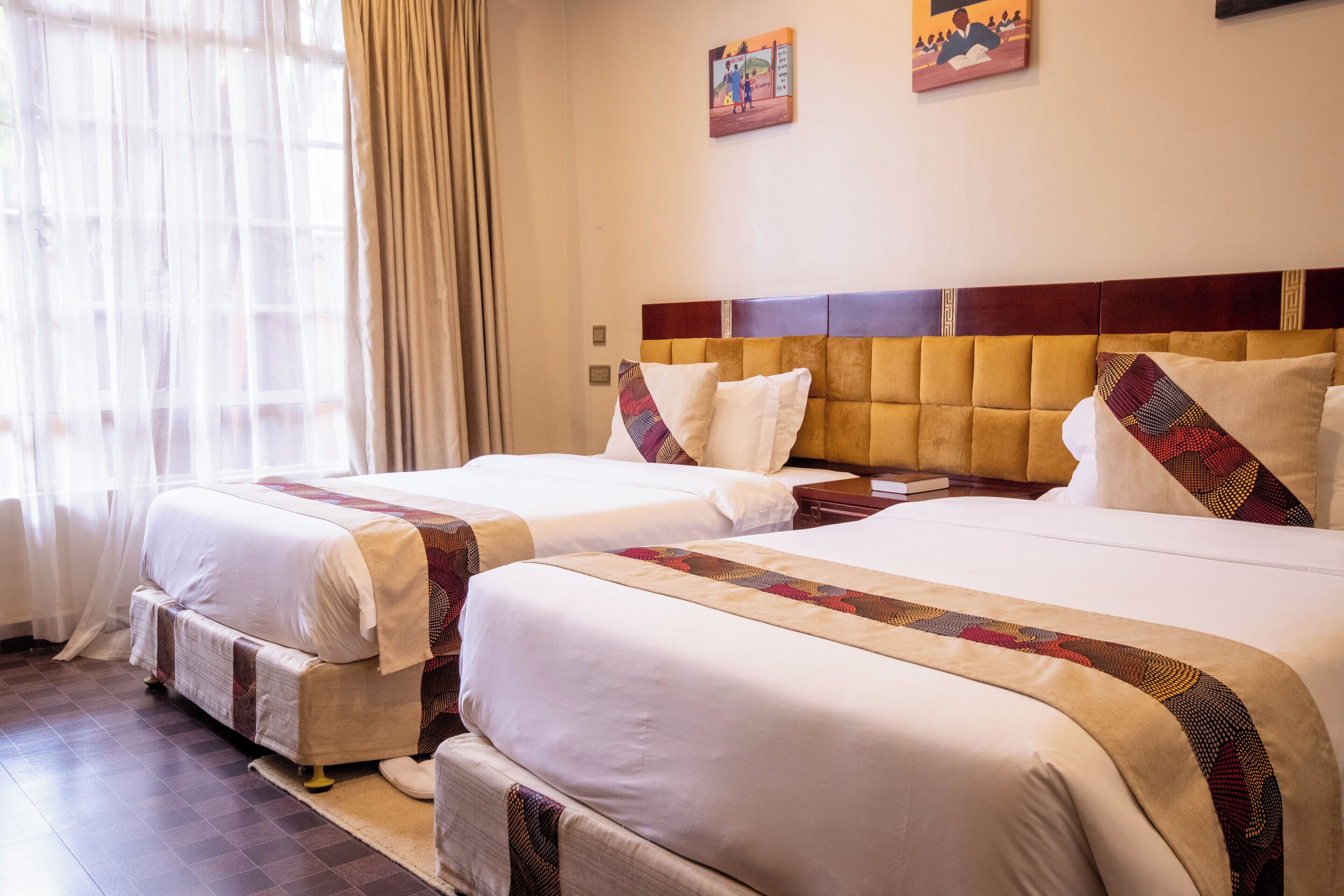 A hotel room with two beds, a wooden headboard, and a large window with sheer curtains.