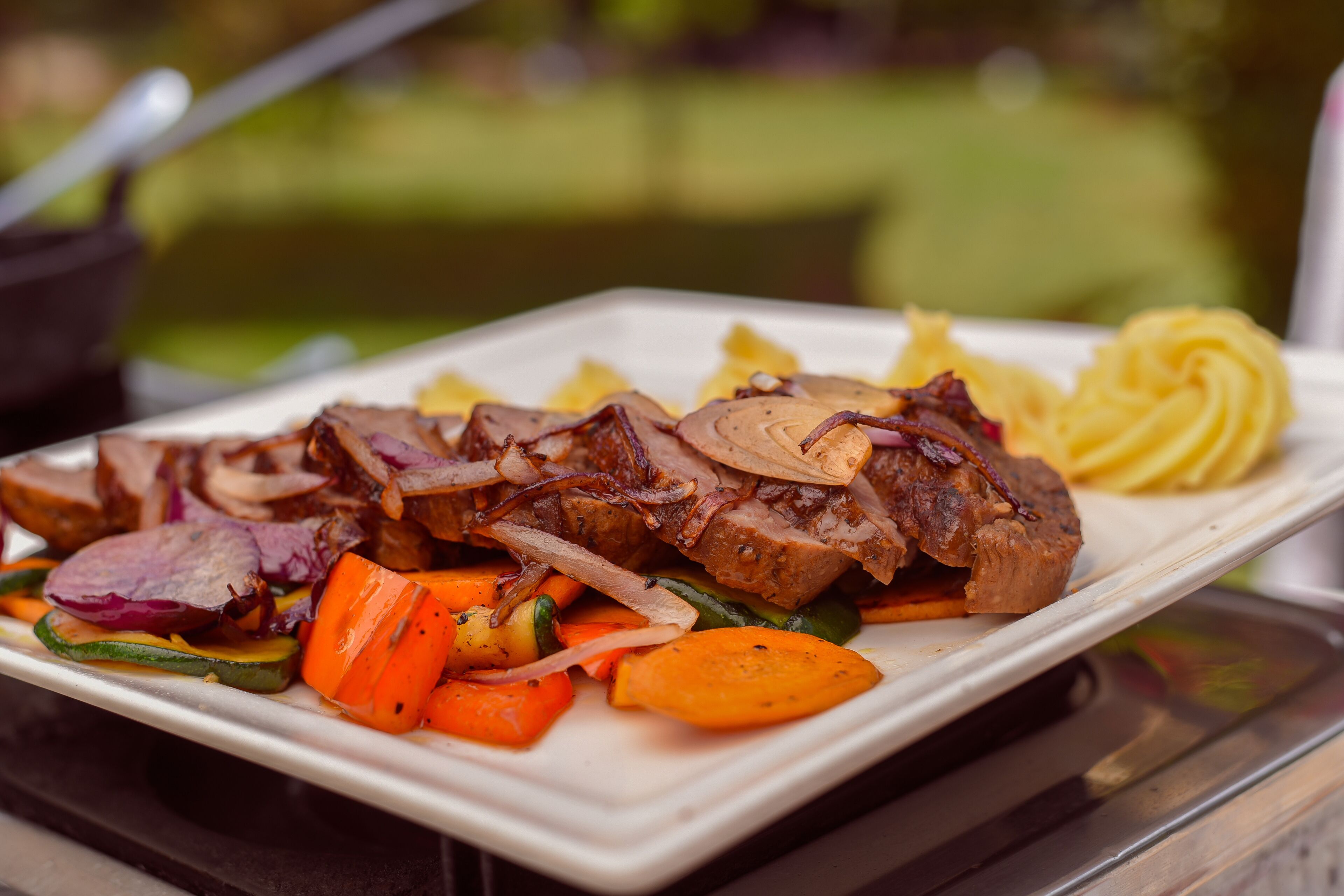 Un piatto di carne a fette con verdure e un giro di salsa.
