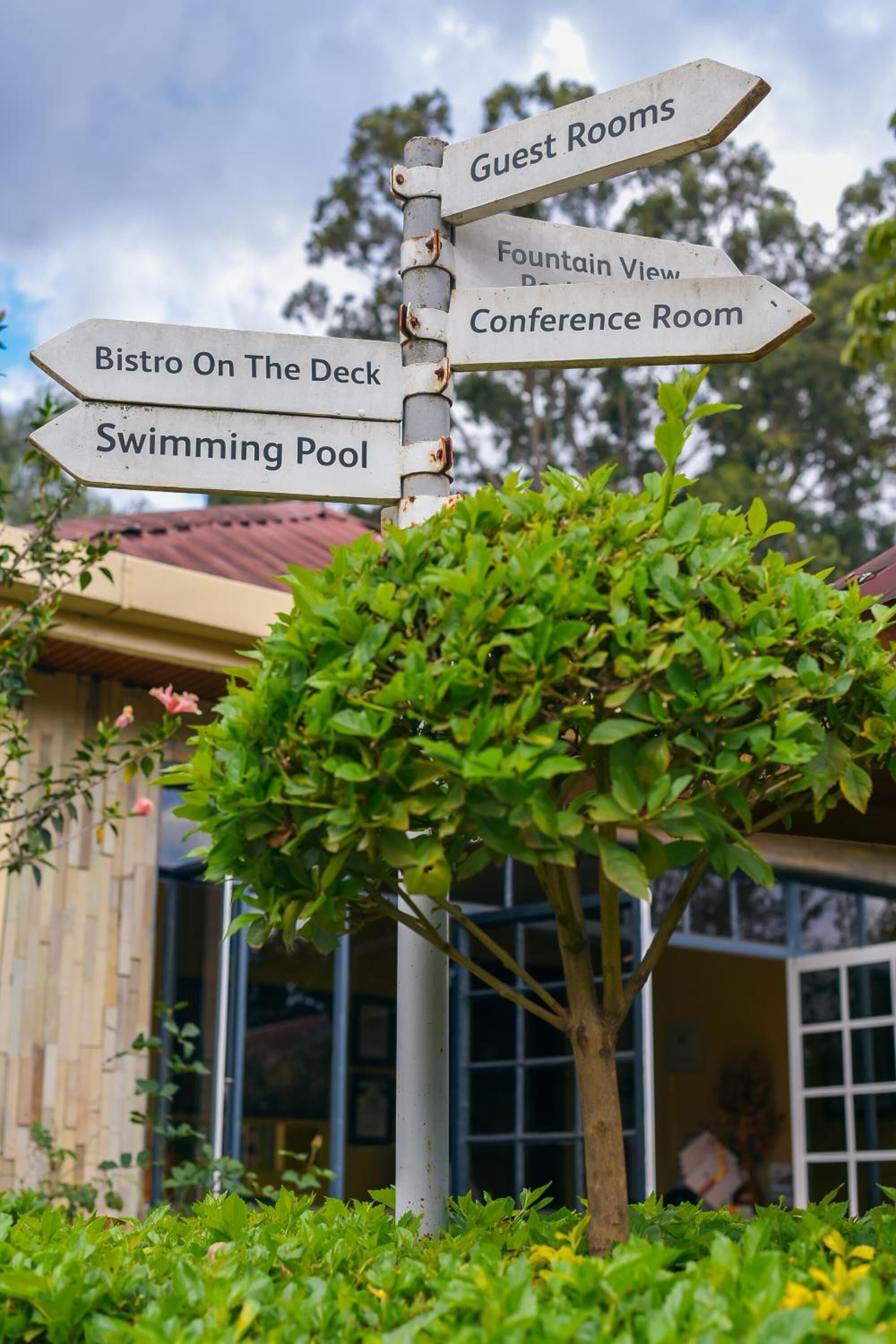 A directional signpost with multiple arrows pointing to amenities such as guest rooms, a fountain view, a conference room, a bistro on the deck, and a swimming pool.