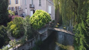 Un edificio junto al río con un puente, rodeado de abundante vegetación y árboles.