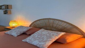 Una cama con almohadas de estampado floral, cabecera de mimbre y una lámpara de noche.