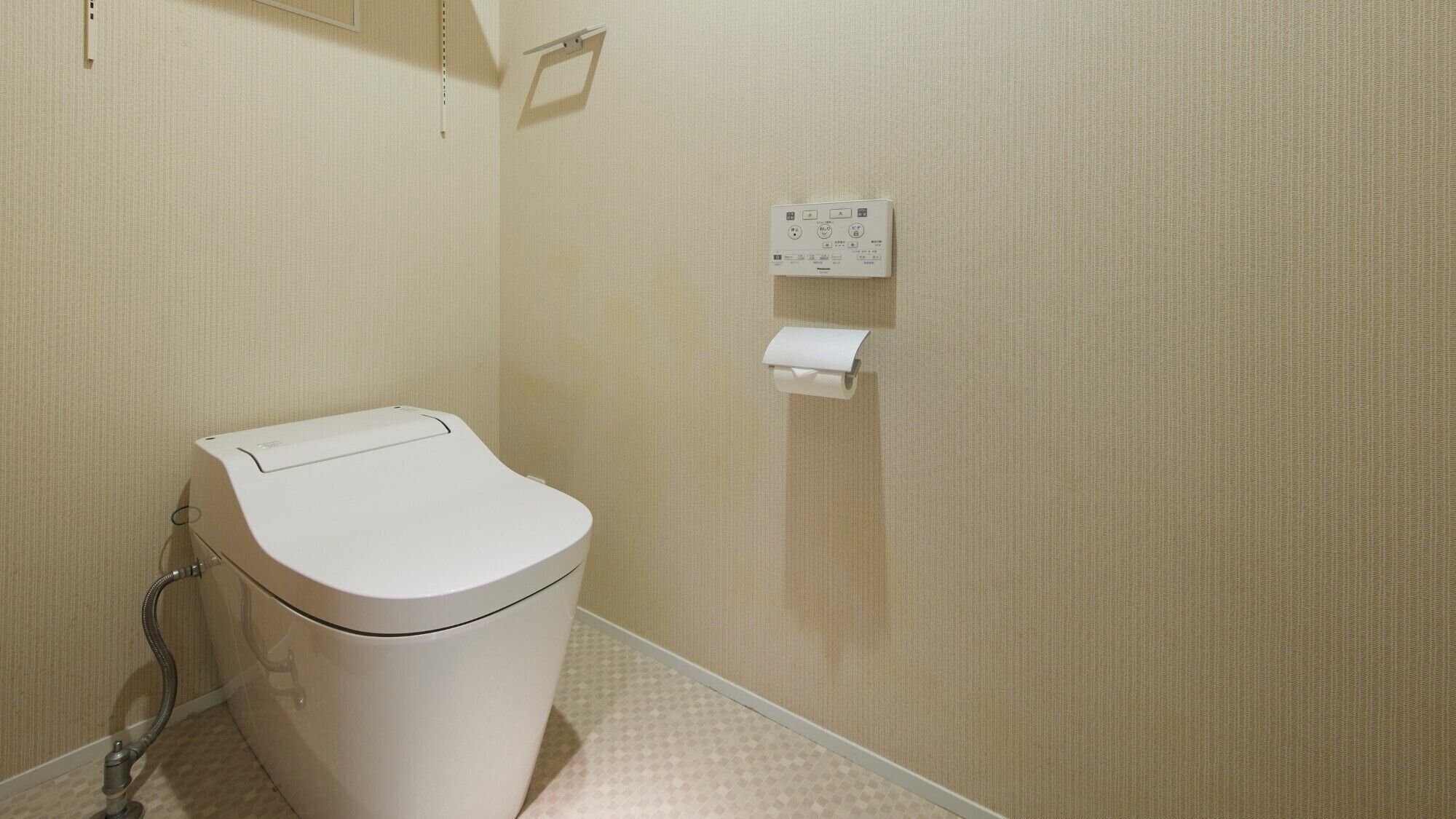 A small bathroom with a toilet, a paper towel dispenser, and a wall-mounted electrical outlet.