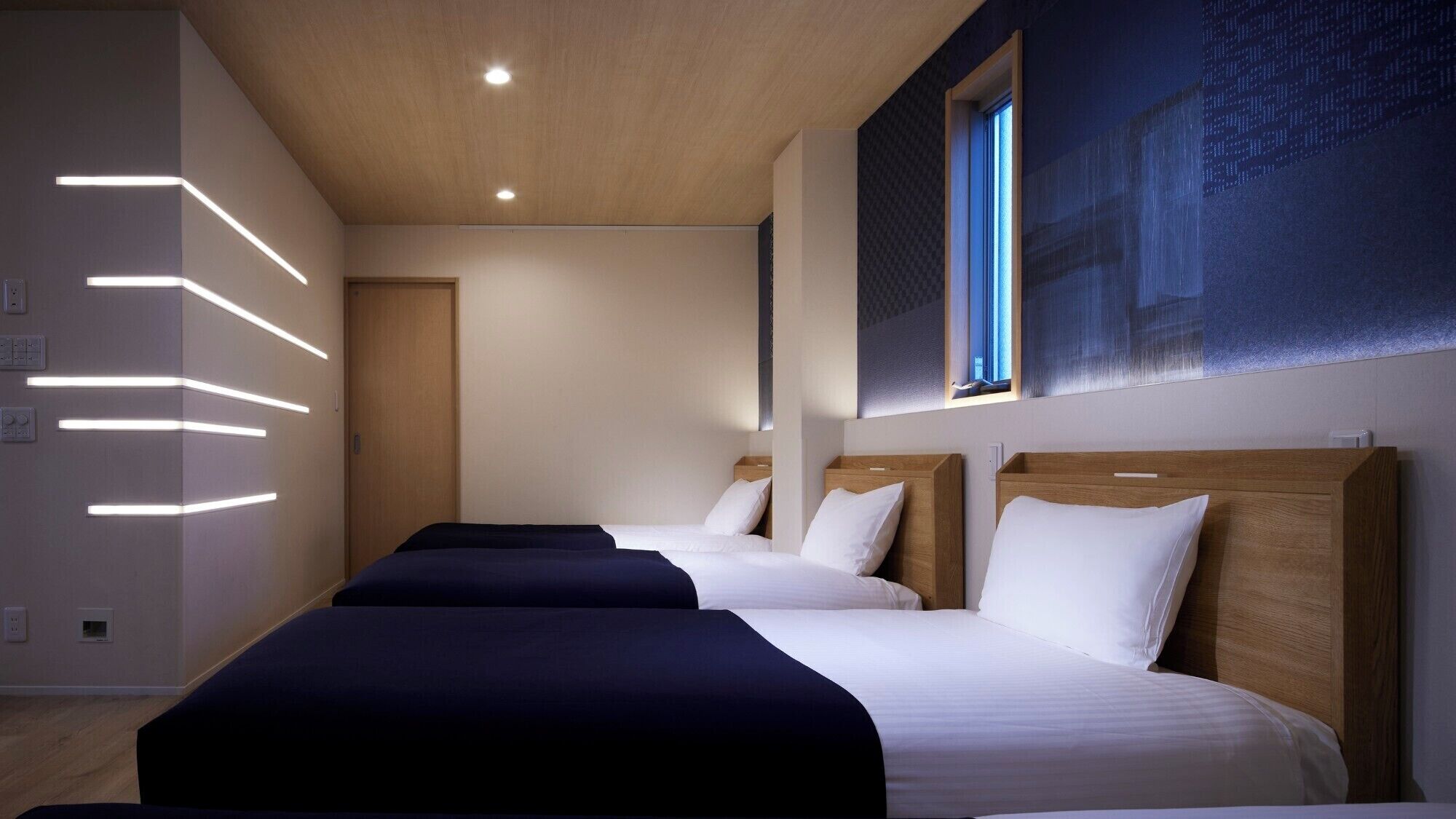 Une chambre d’hôtel avec trois lits, des têtes de lit en bois et une grande fenêtre.