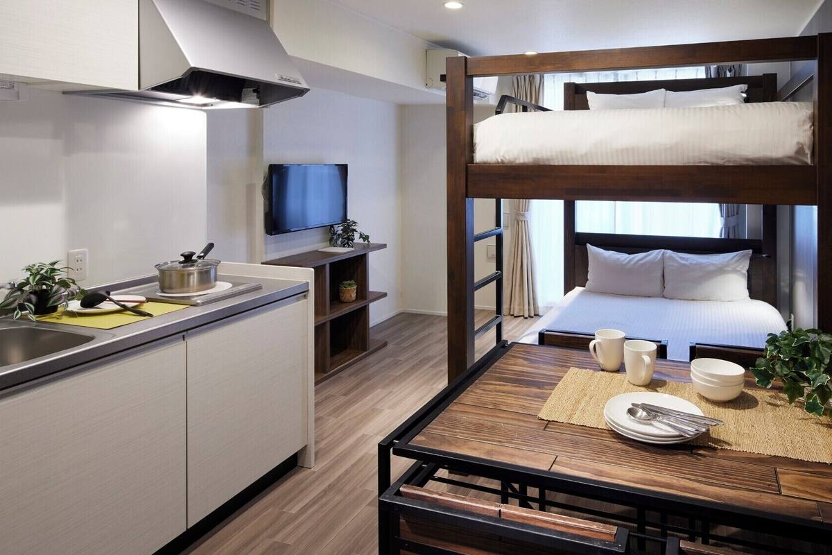 Una habitación de hotel compacta con literas, kitchenette y un pequeño comedor.