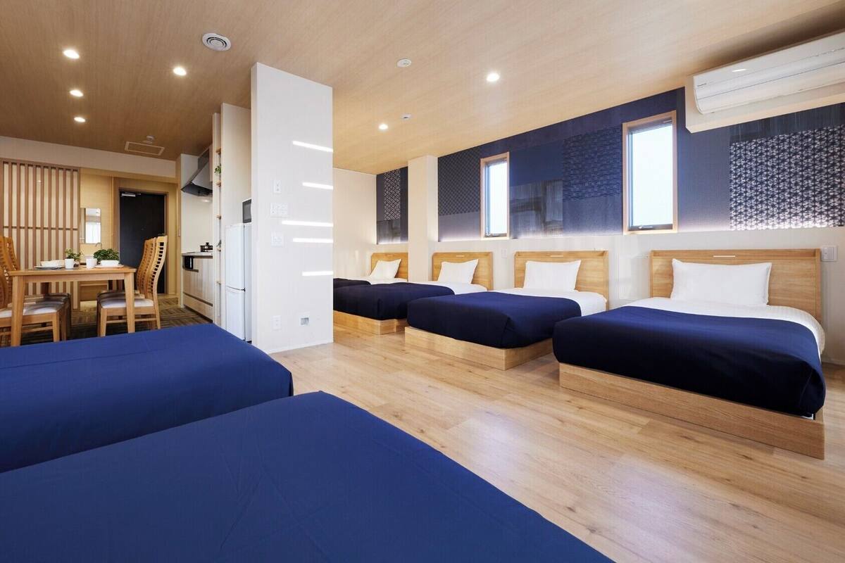 Habitación de hotel con cuatro camas individuales, un comedor con mesa y sillas, y una kitchenette.