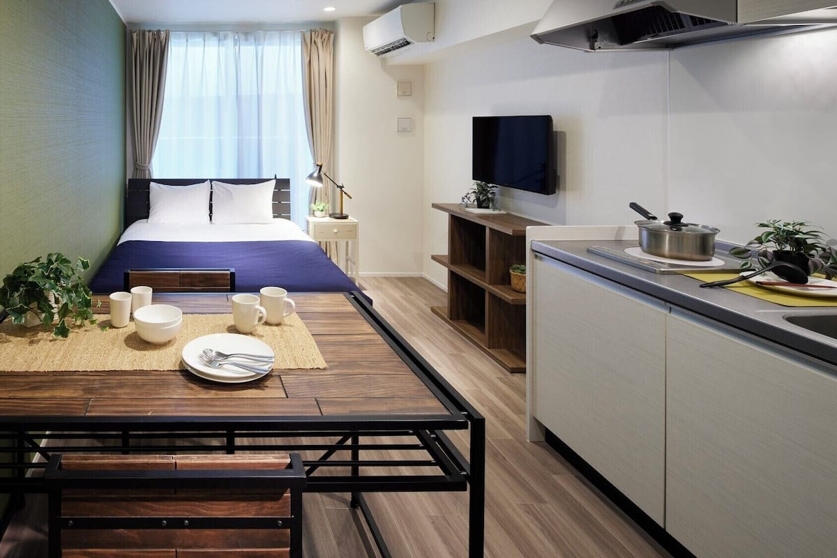 Habitación de hotel compacta con cama, mesita de noche y kitchenette.
