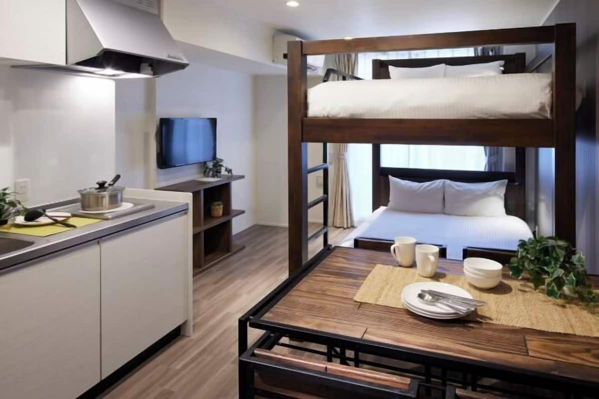 Habitación de hotel compacta con literas, kitchenette pequeña, mesa de comedor y televisión.