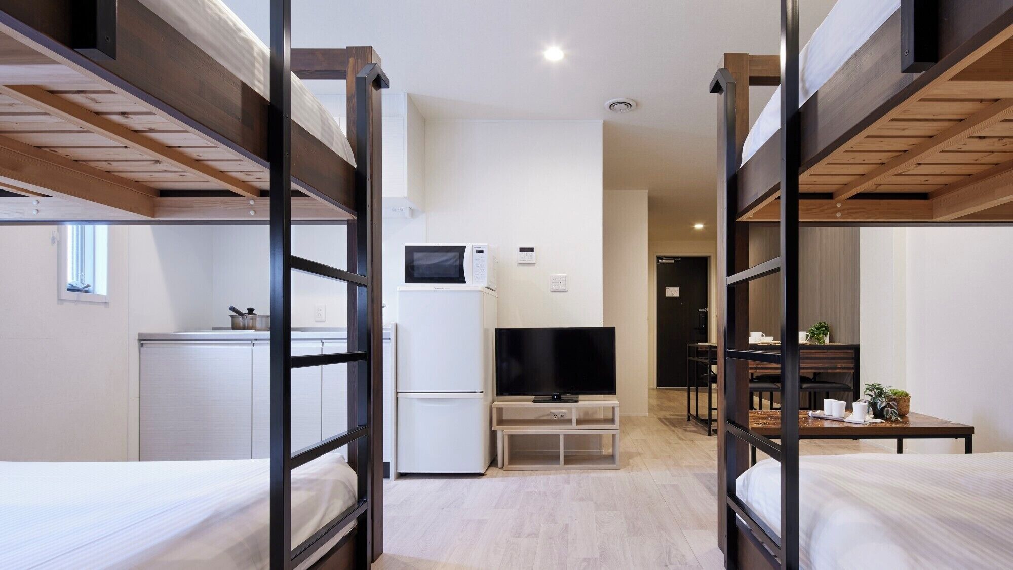 A compact hotel room with bunk beds, a kitchenette, a TV, and a small dining area.