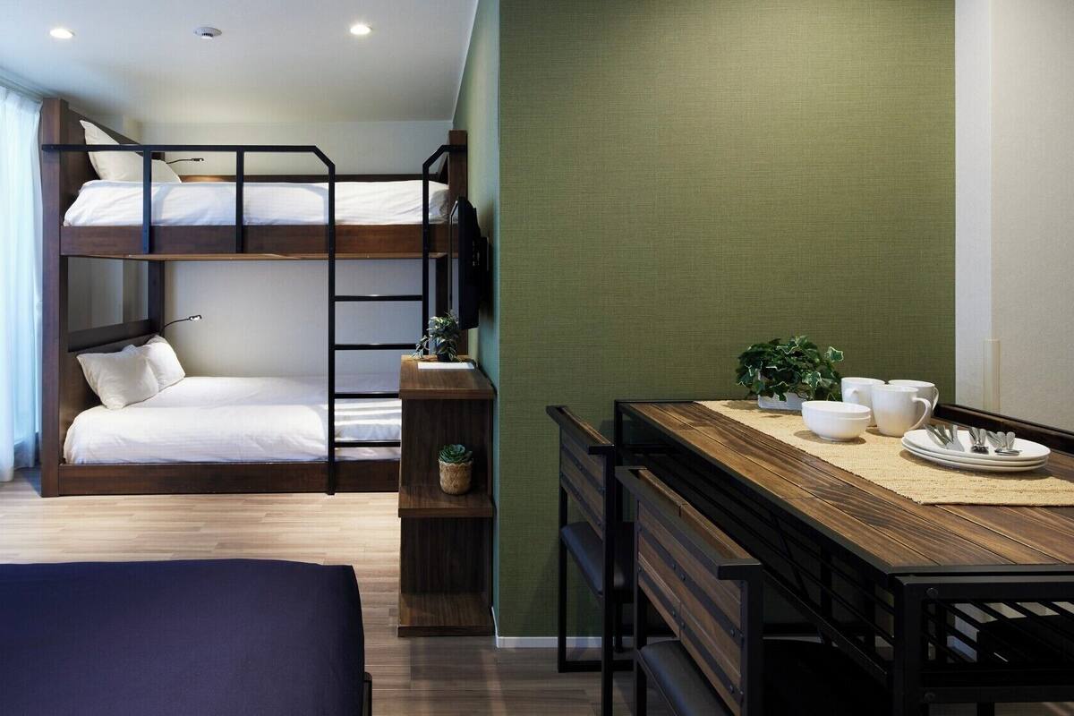Habitación con literas, una mesa de madera y sillas, una planta pequeña y una ventana con cortinas.