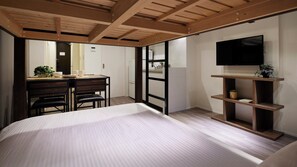 Ein Schlafzimmer mit einem großen Bett, einem Schreibtisch mit Stühlen, einem Fernseher auf einem Regal und einer Schiebetür zum Badezimmer.