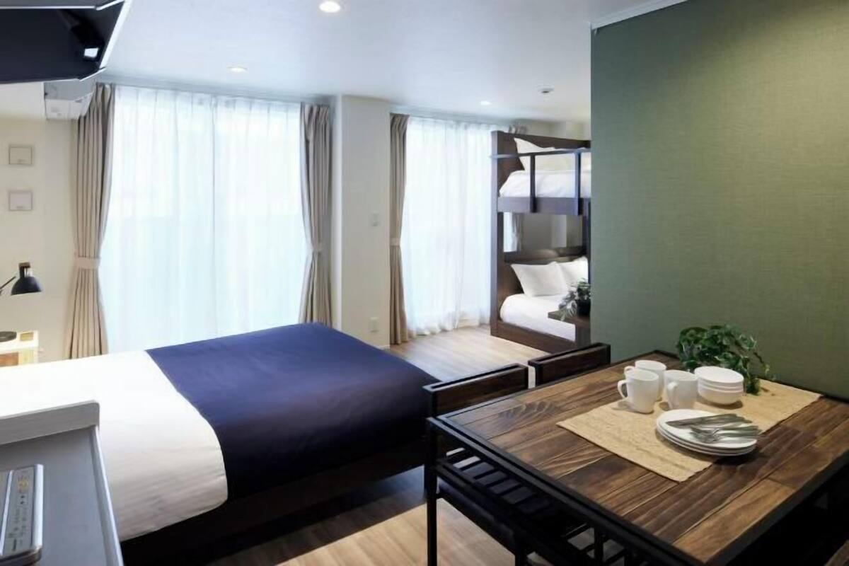 Habitación de hotel con cama, escritorio, y una mesa con una bandeja de platos y tazas, además de una planta.