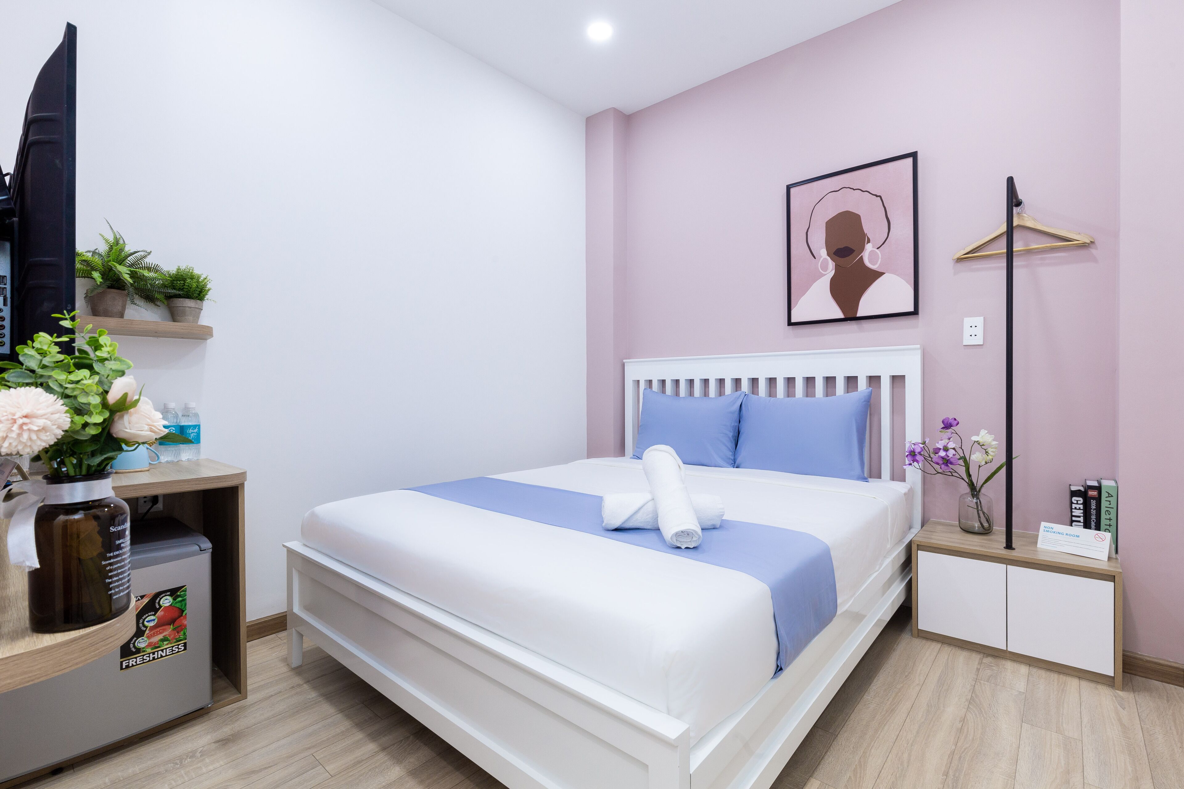 Een keurig ingerichte hotelkamer met een bed, nachtkastjes, een televisie en een klein plankje met planten en een vaas.