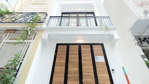 A building with a white facade, a wooden door, and a balcony with metal railings. - Cozrum Homes Charming Corner (Ho Chi Minh City)