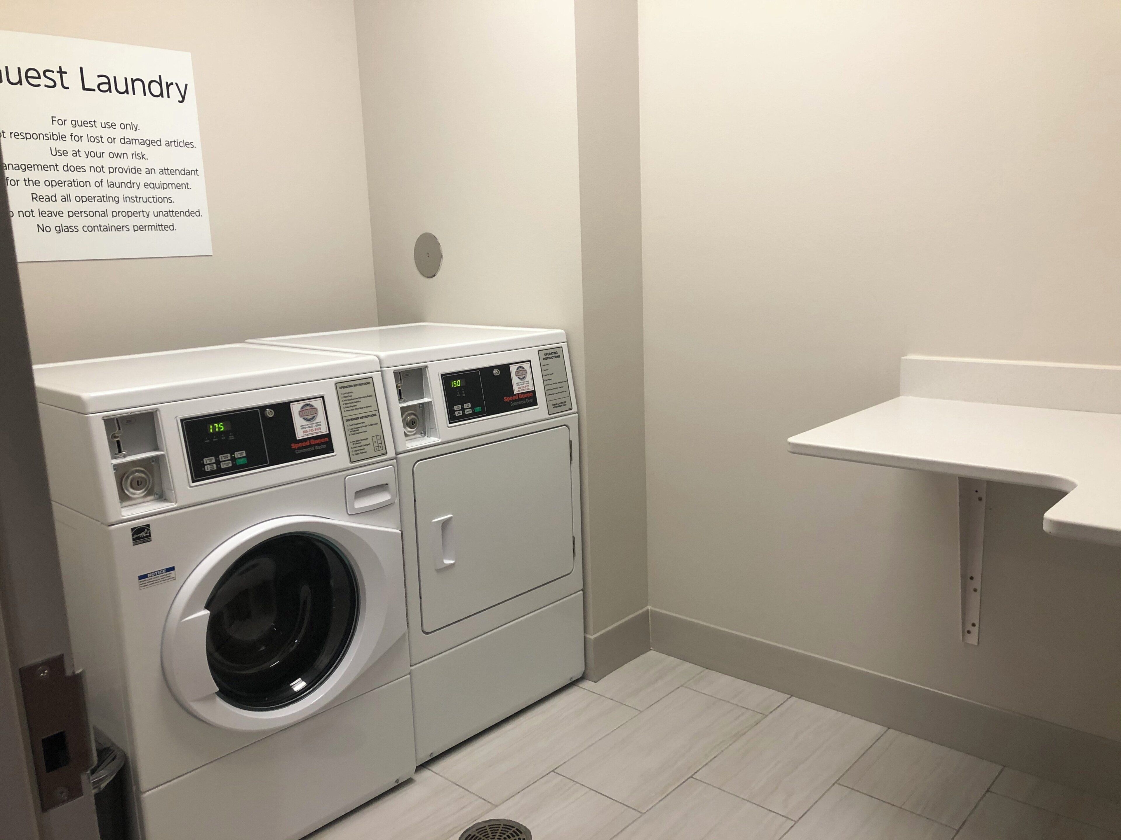 A laundry area with two front-loading washing machines, a wall-mounted sink, and a sign detailing laundry rules.